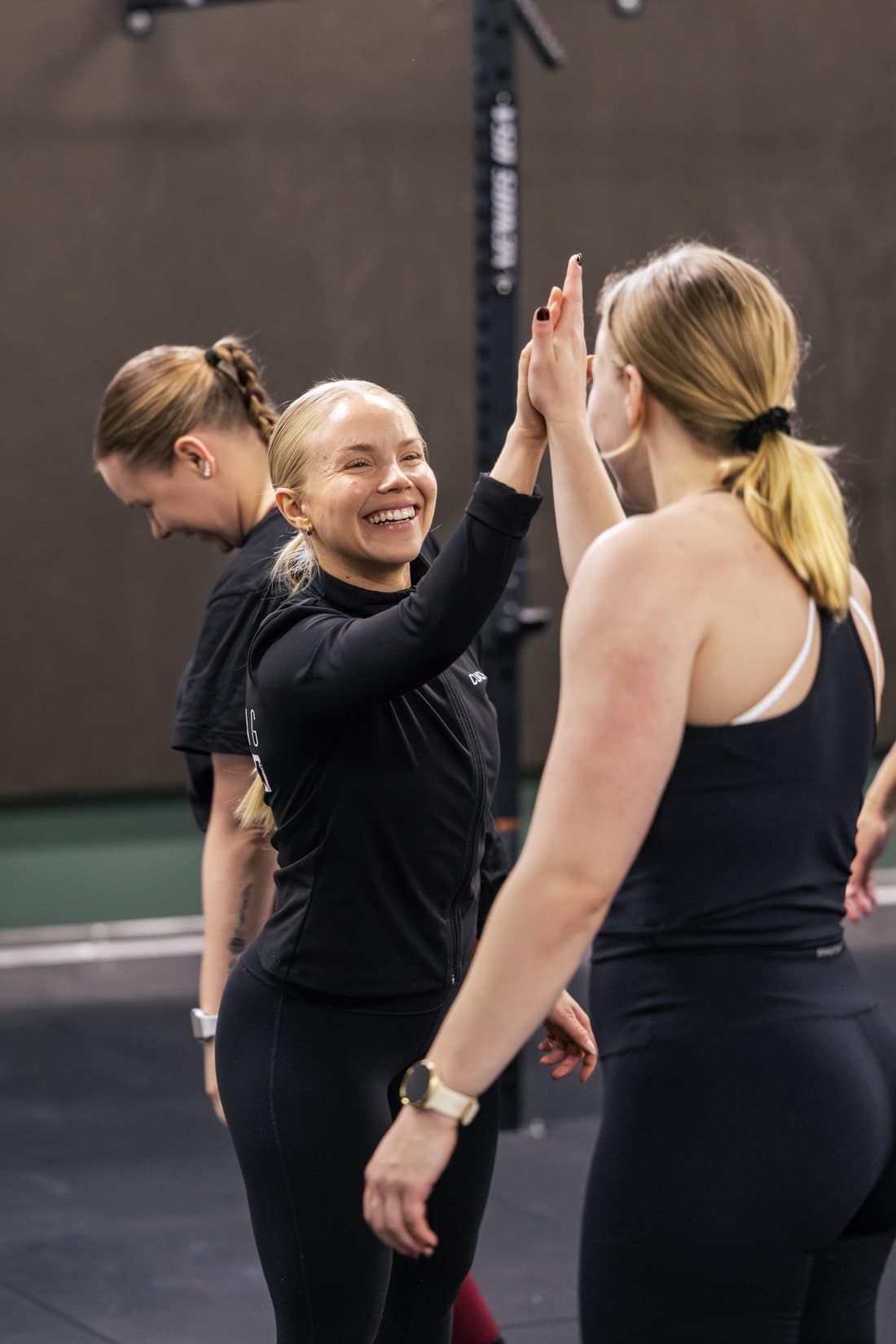 Hymyilevä treenaaja antaa ylävitosen toiselle treenaajalle CrossFit-tunnilla.