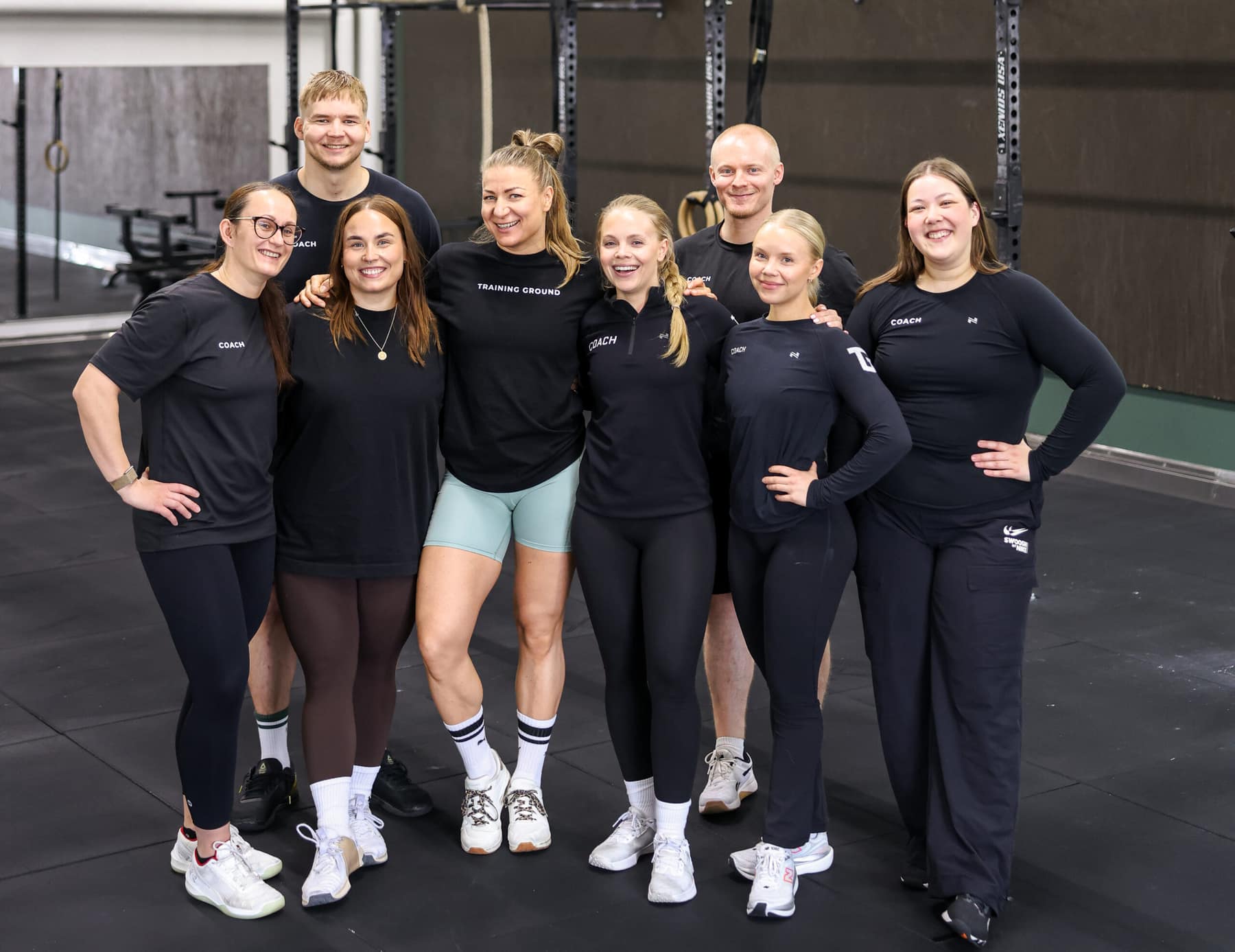 Training Groundin valmentajat ryhmäkuvassa salilla, hymyillen ja toisiaan halaten.